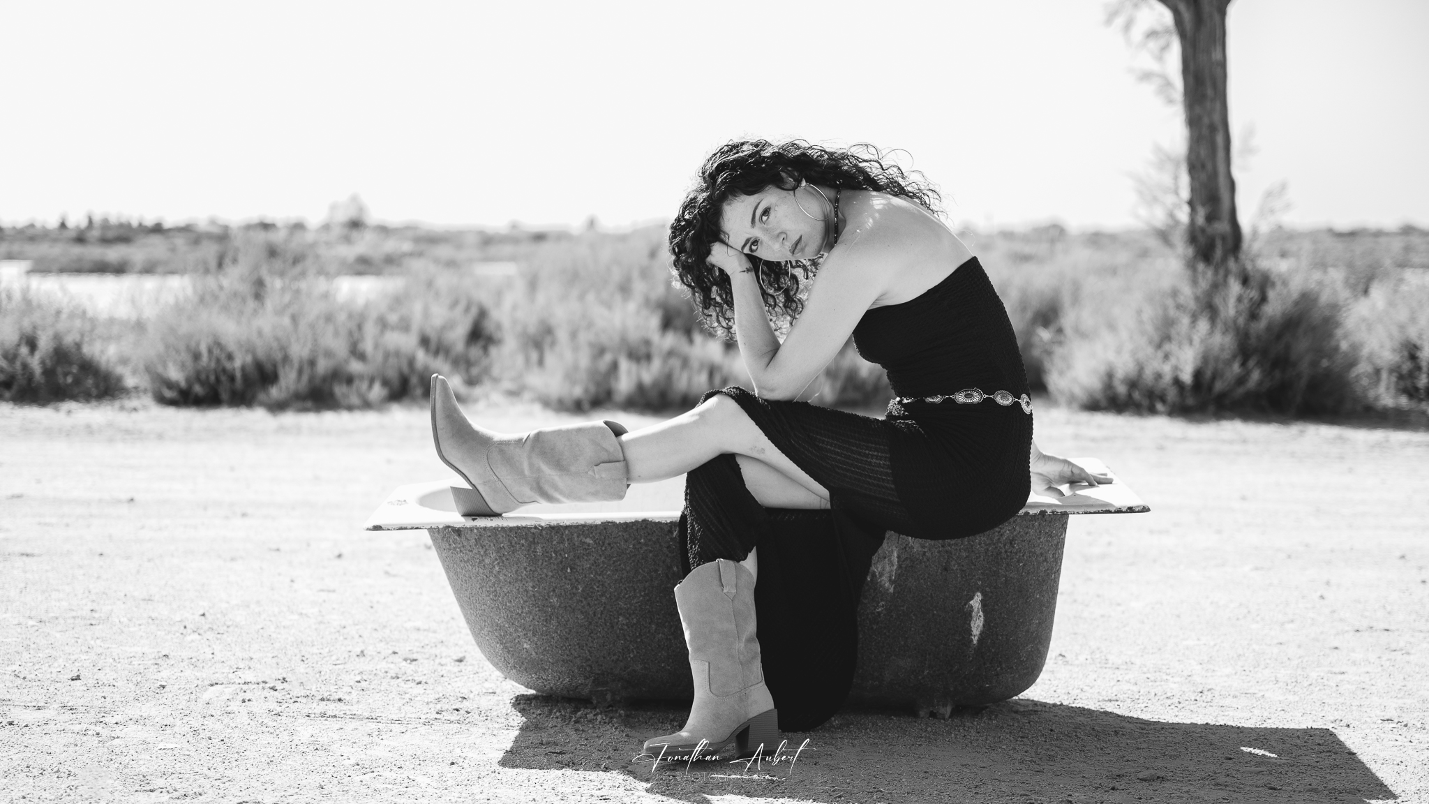 Portrait en noir et blanc d'une femme assise sur un bloc de béton, paysage désertique de Camargue en arrière-plan