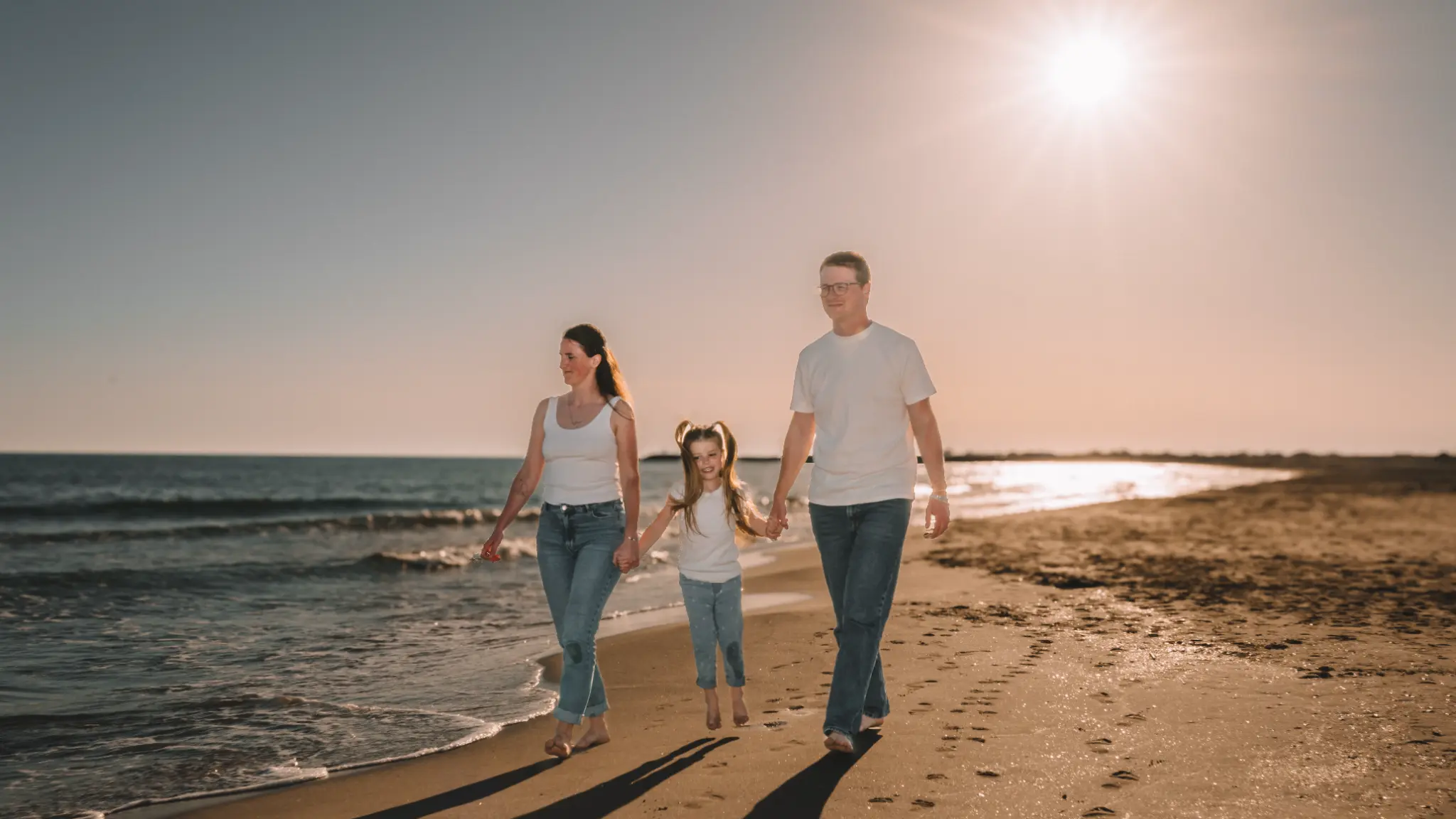 Séance photo de famille sur la plage au coucher de soleil, parents et enfant marchant dans l'eau